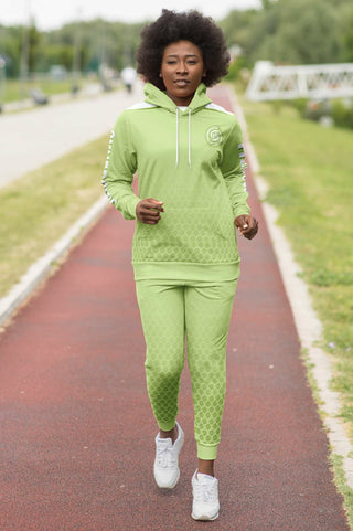 A woman jogging on a track wears a stylish lime green Synergetic Heroes hoodie and joggers. The athletic outfit is perfect for fitness, running, and active lifestyles.