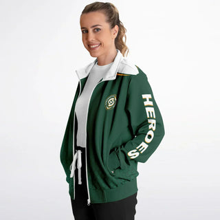 Smiling woman in a green Synergetic Heroes track jacket with bold sleeve branding, standing against a white background. This stylish, comfortable athleisure jacket is perfect for casual wear, workouts, and active lifestyles. Shop Synergetic Heroes!