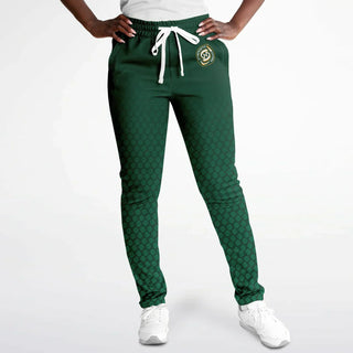 Woman wearing green Synergetic Heroes track pants with a drawstring waist and branding, posing against a white background. These stylish, comfortable joggers are perfect for workouts, casual wear, and active lifestyles. Shop Synergetic Heroes apparel!